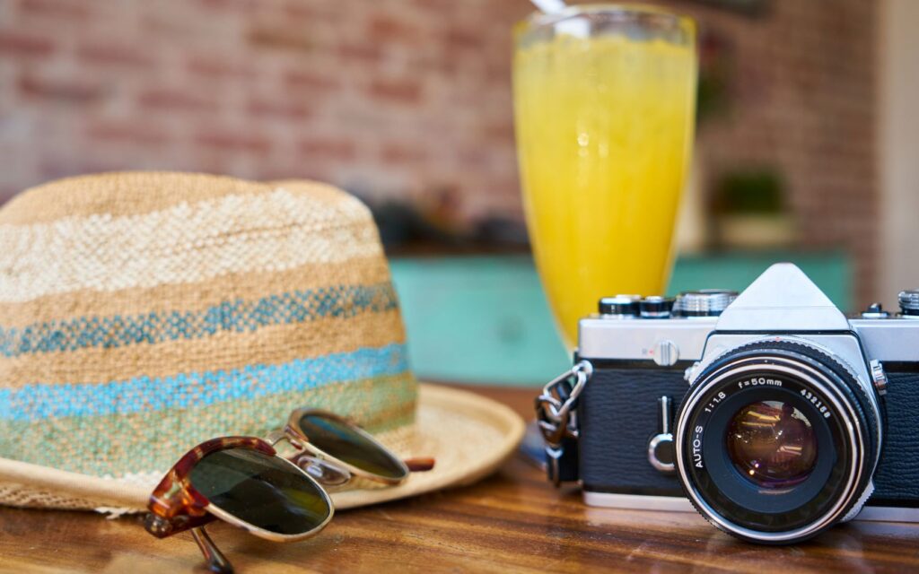 Stock photo of vacation-related objects: straw hat, sunglasses, camera, and an orange-colored iced drink